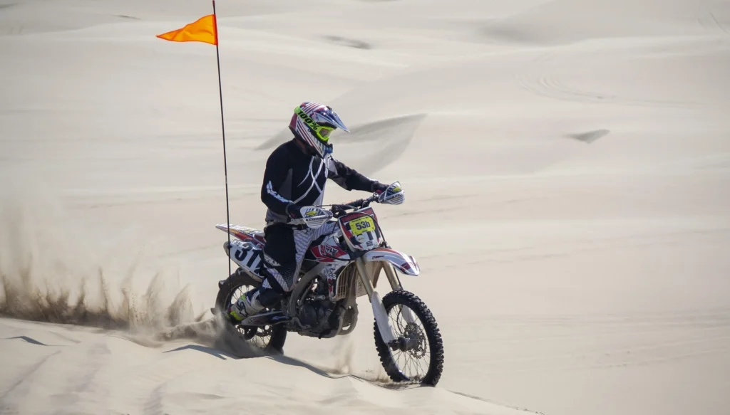 Motocross rider in black gear navigating white desert dunes