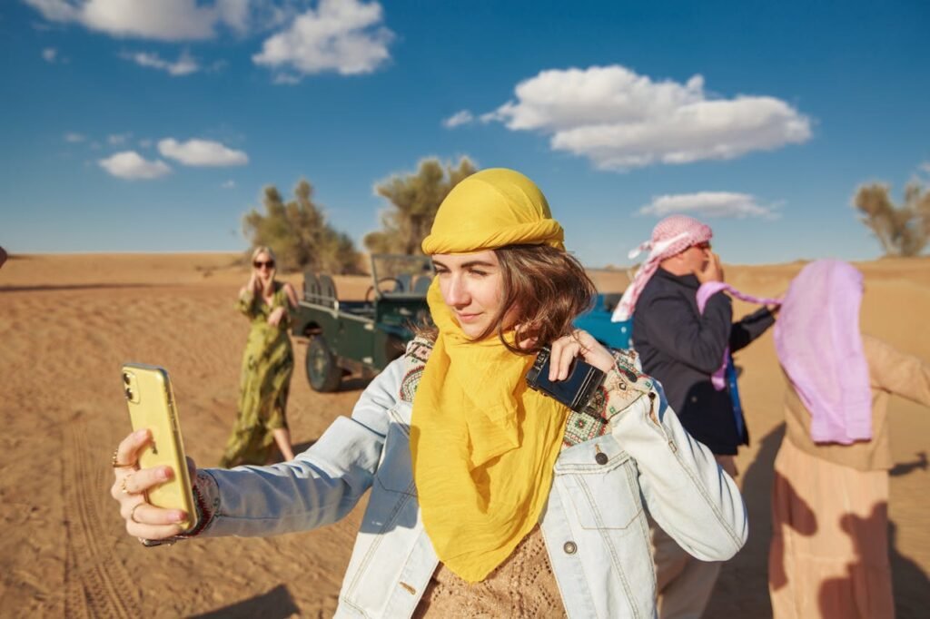 A woman taking a selfie in the desert while wearing a yellow headscarf and light denim jacket, showing an example of what to wear in Dubai desert safari for comfort and sun protection.